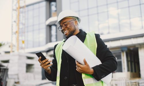 Young black race man with blueprint stading near glass building. Talking by phone.